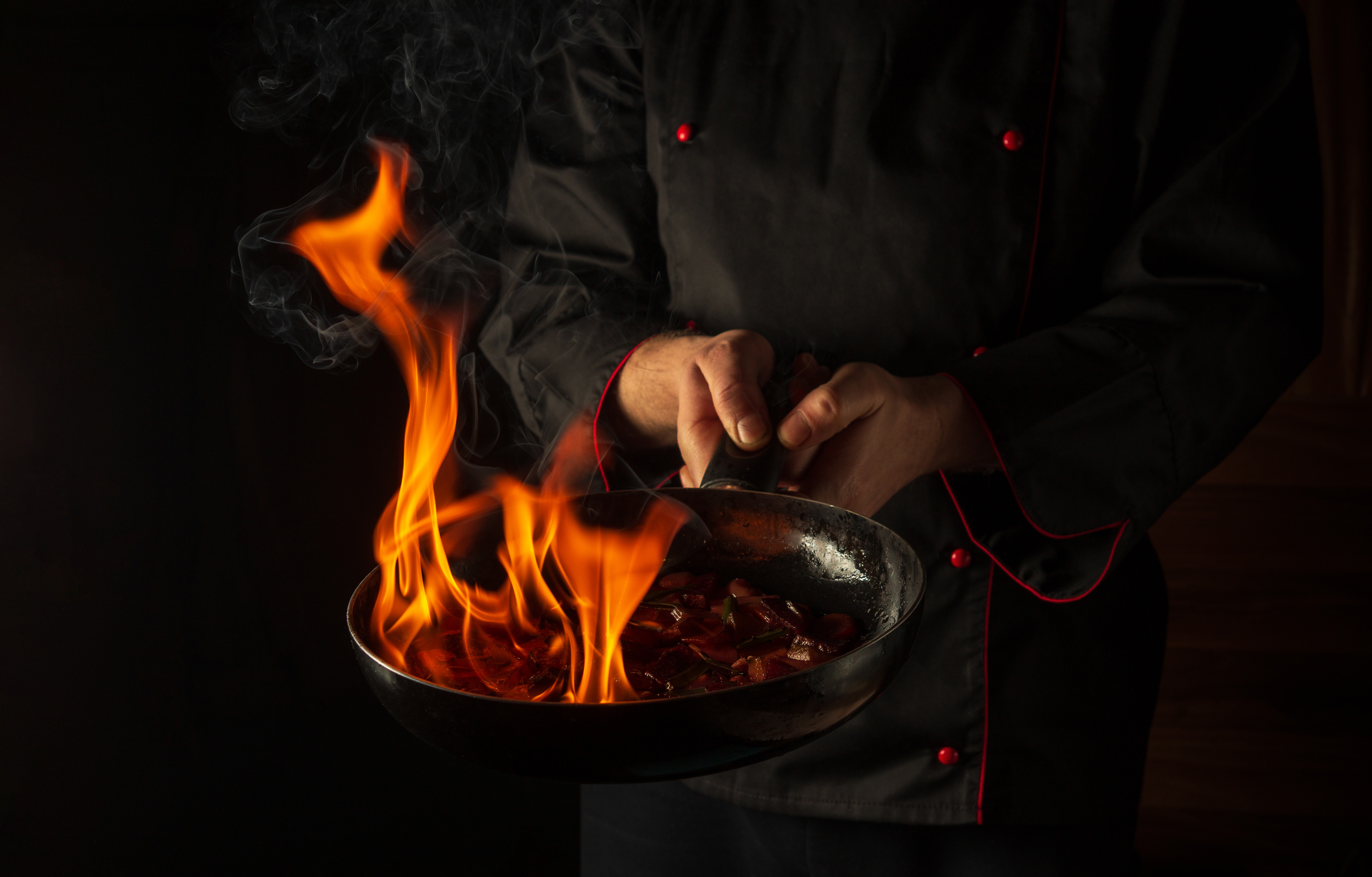 Chef prepares vegetable food in a frying pan with a flame of fire. The concept of restaurant and hotel service. Flamber or cooking over natural fire. Grande cuisine